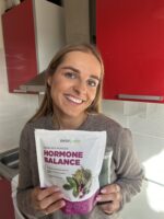 Moteris laiko Hormonų pakuotę ir šypsosi i kamerą